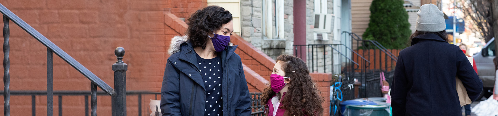 Mother and daughter holding hands and looking at each other. They're both wearing face masks 