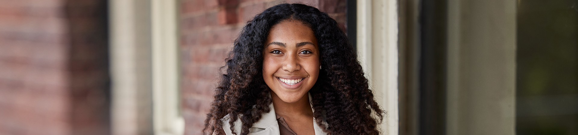  Portrait of ambassador girl scout wearing vest and smiling at camera in front of a brick building. 